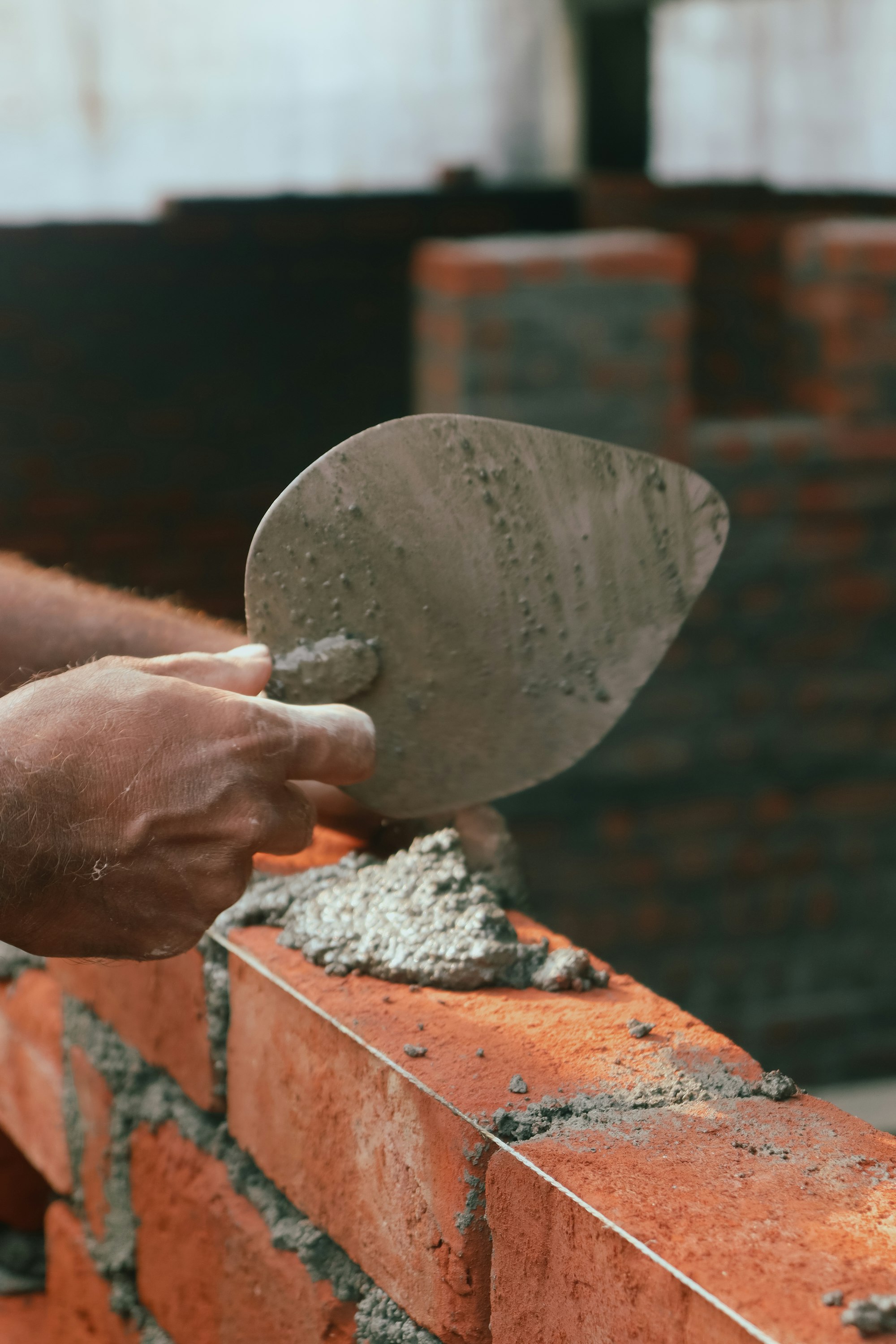 Bricklayer spreading mortar with a trowel on a course of red facing brick